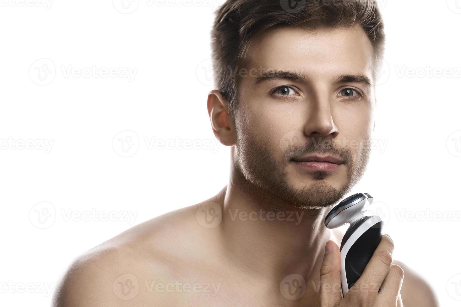 Handsome man is using electric shaver on white background photo