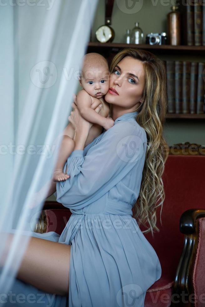 joven y hermosa madre con un vestido gris de lujo sosteniendo a su bebé en las manos foto