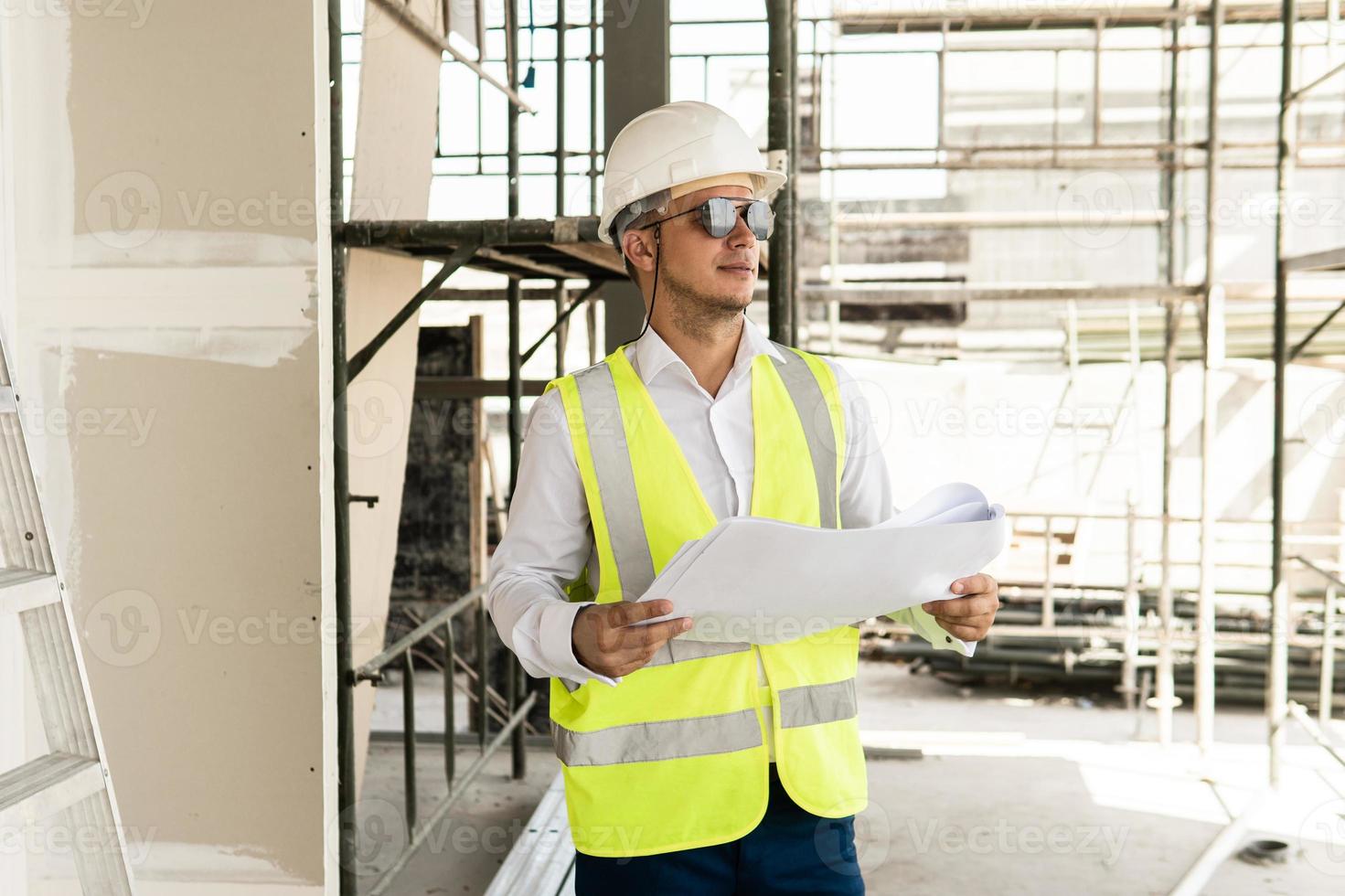 Man architect wearing safety vest with a blueprints on a construction site photo