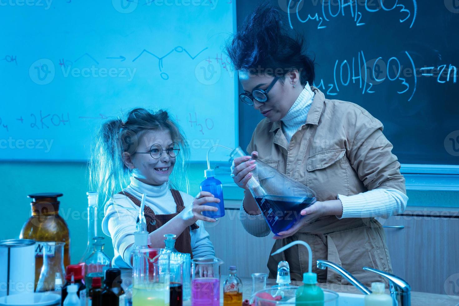 Teacher and little girl during chemistry lesson mixing chemicals in a