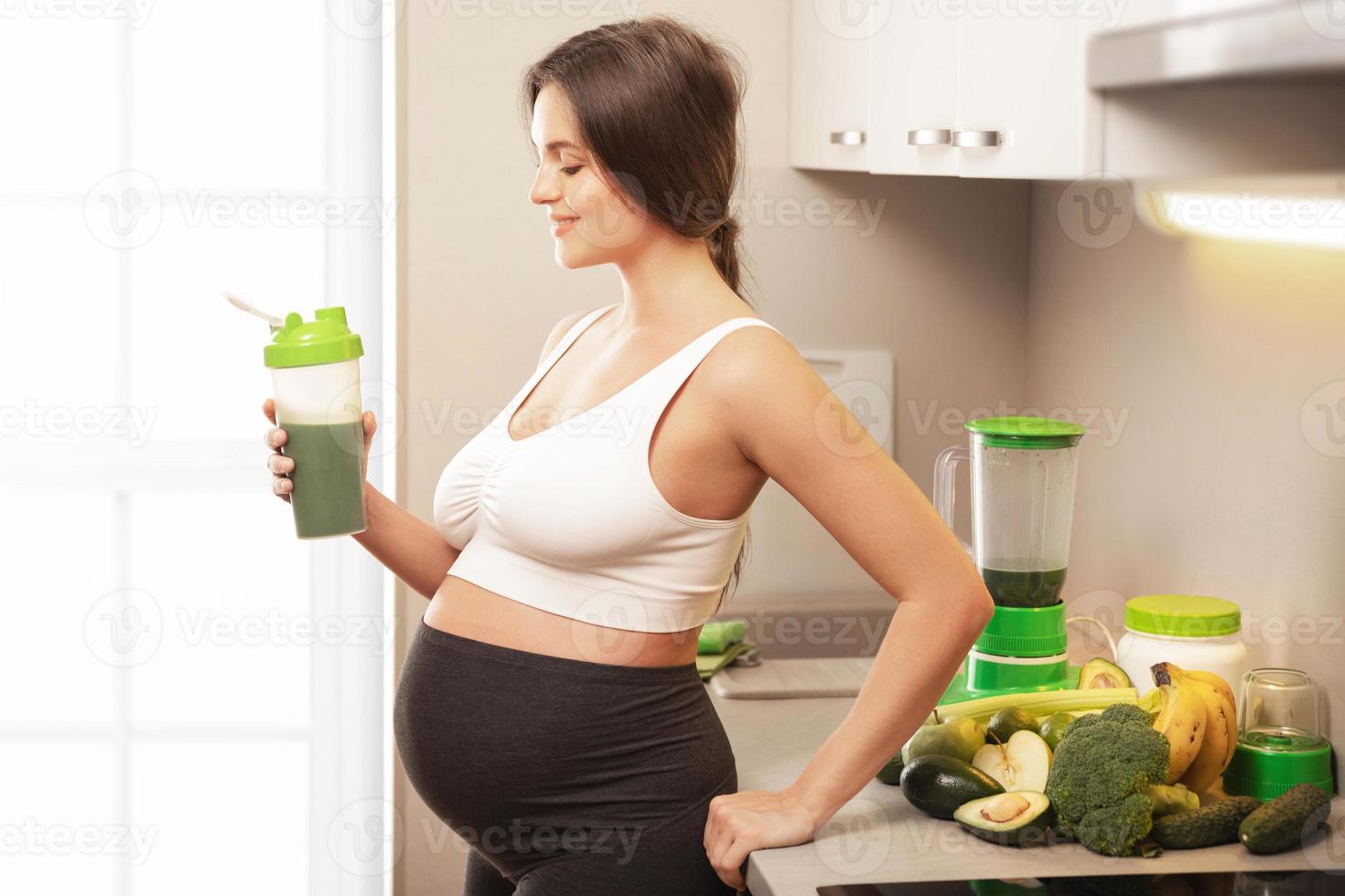 mujer embarazada sosteniendo un agitador con un cóctel de proteína verde foto