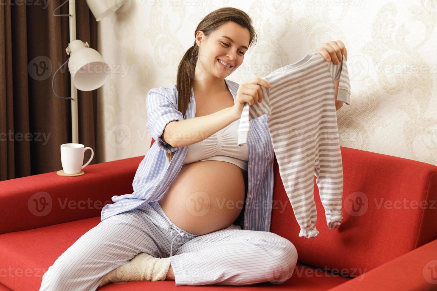 Young pregnant woman looking at bodysuit for her baby photo