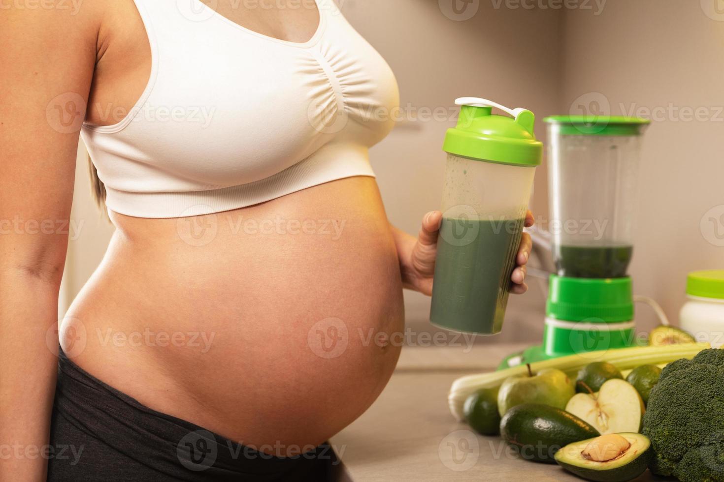 mujer embarazada sosteniendo un agitador con un cóctel de proteína verde foto