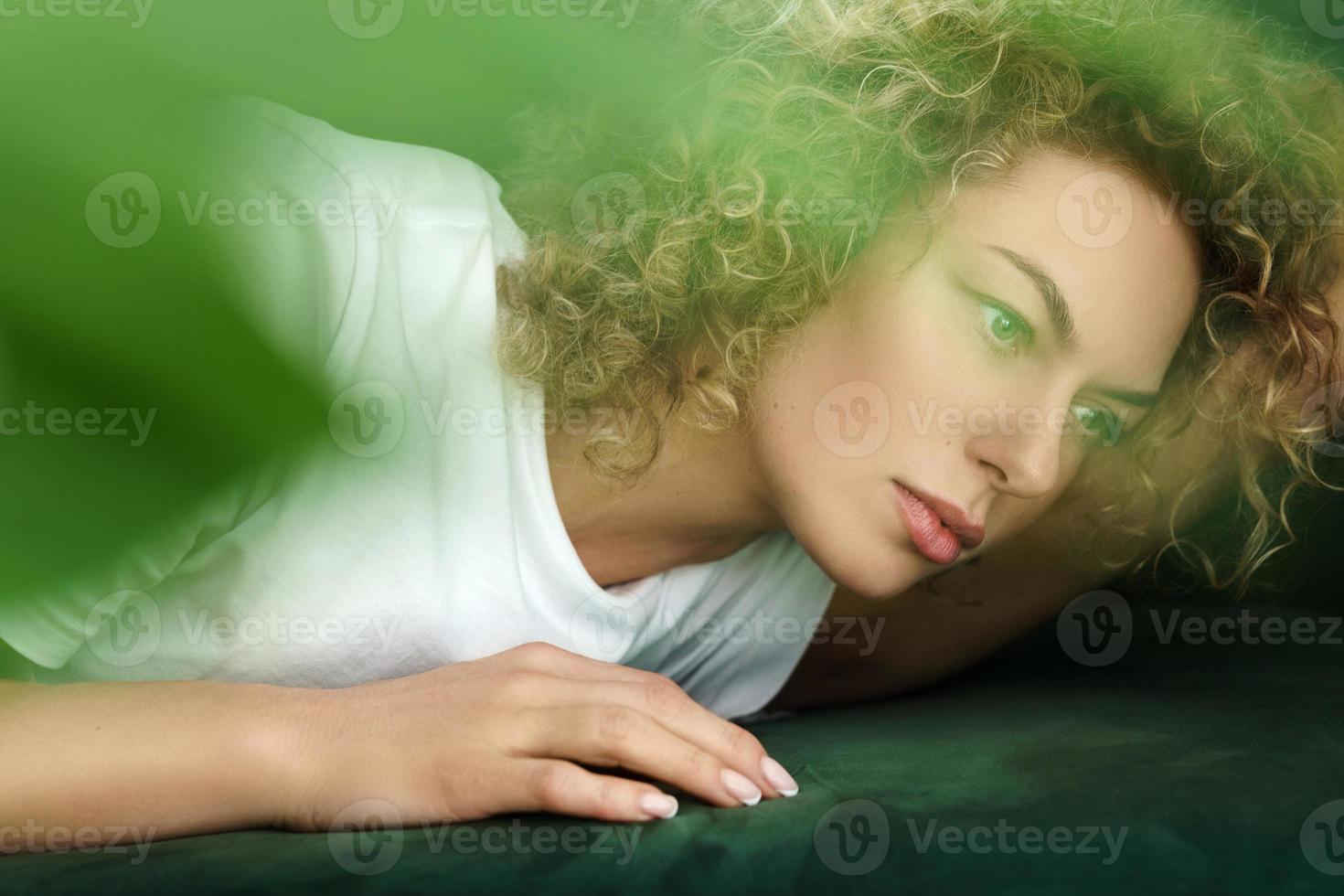 Beautiful woman with curly hair lying on green sofa photo