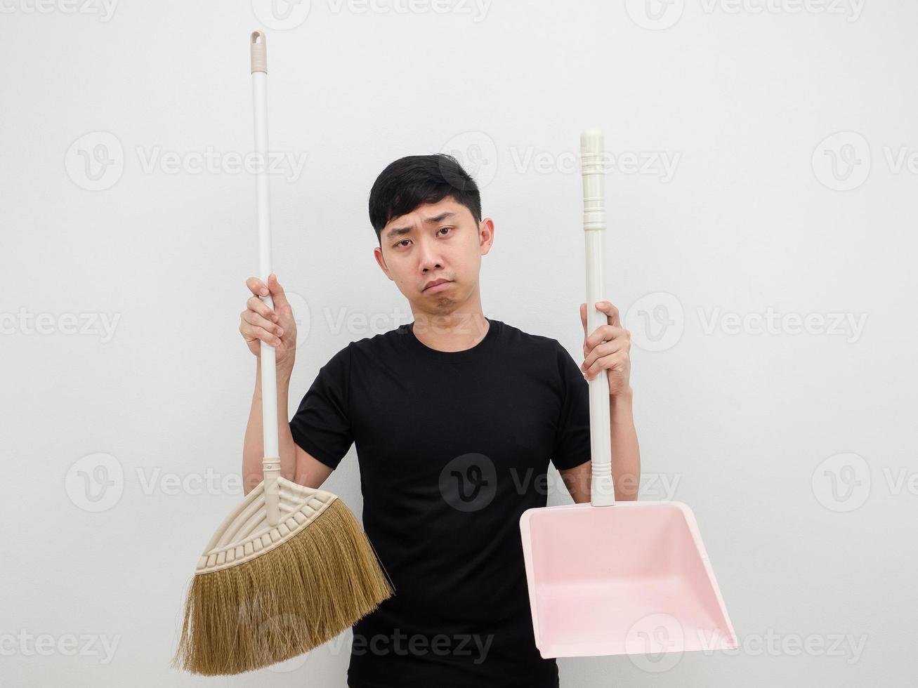 hombre asiático sosteniendo un recogedor y una escoba sintiéndose aburrido de limpiar la casa con fondo blanco foto