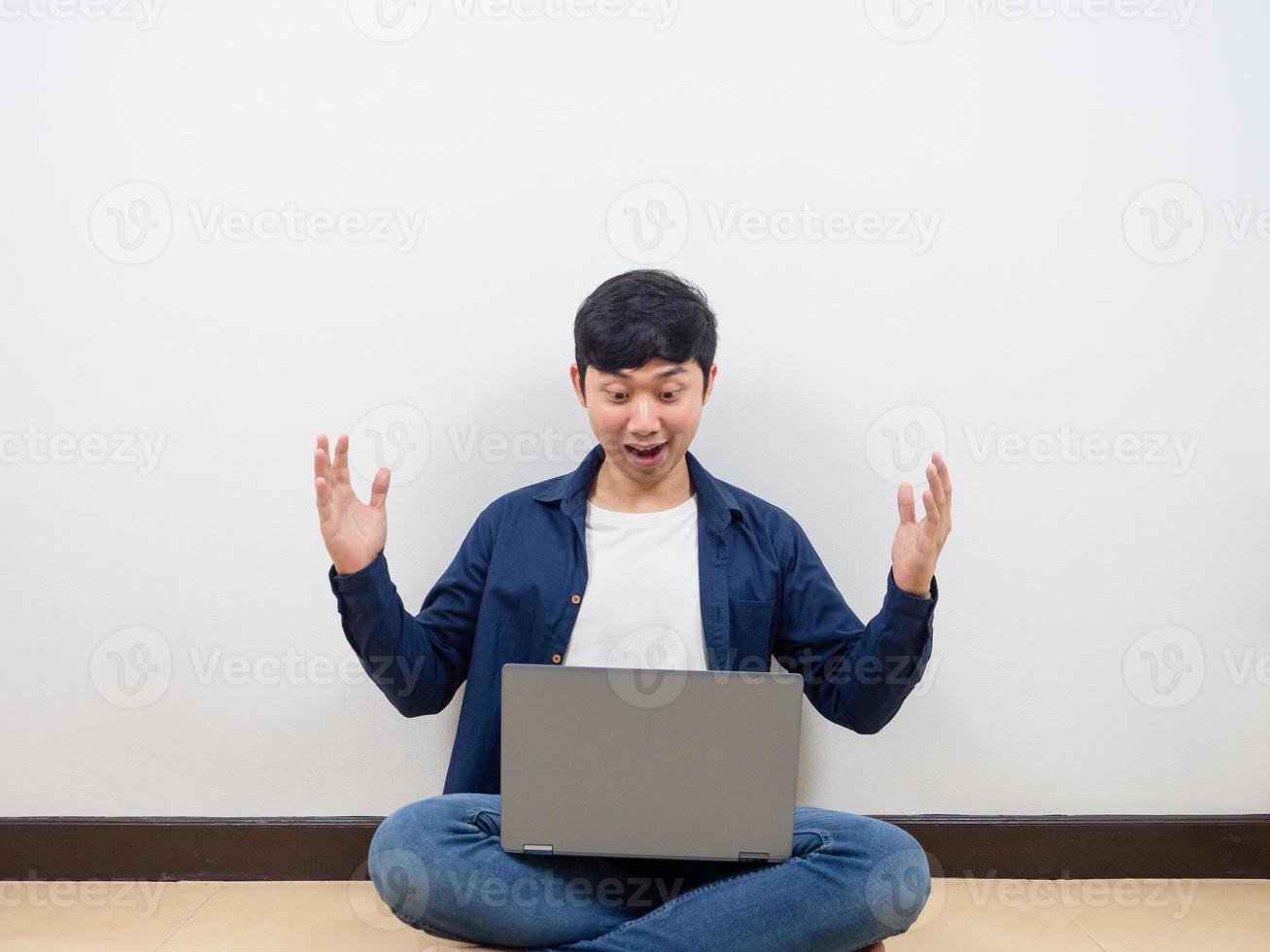 Asian man looking at his laptop feeling happy sitting on the floor photo