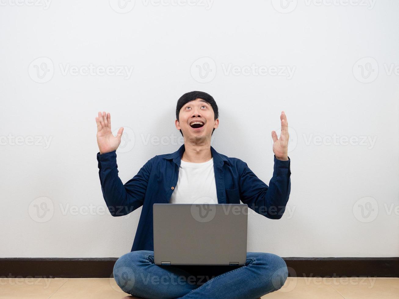 Asian man with laptop cheerful and feeling happy looking up at space sitting on the floor photo