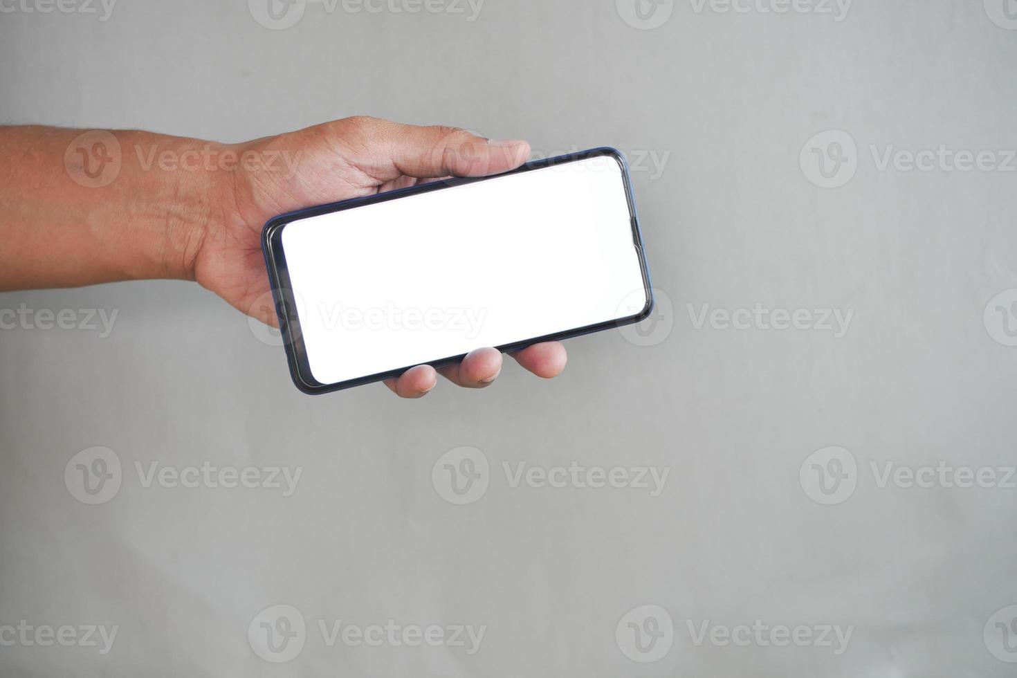 sosteniendo un teléfono inteligente con pantalla vacía sobre fondo gris foto