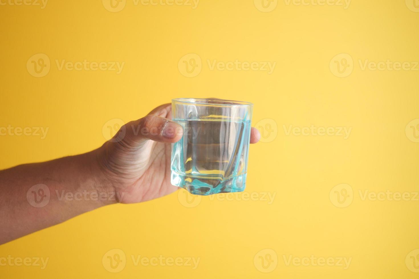 holding a glass of water against yellow background photo