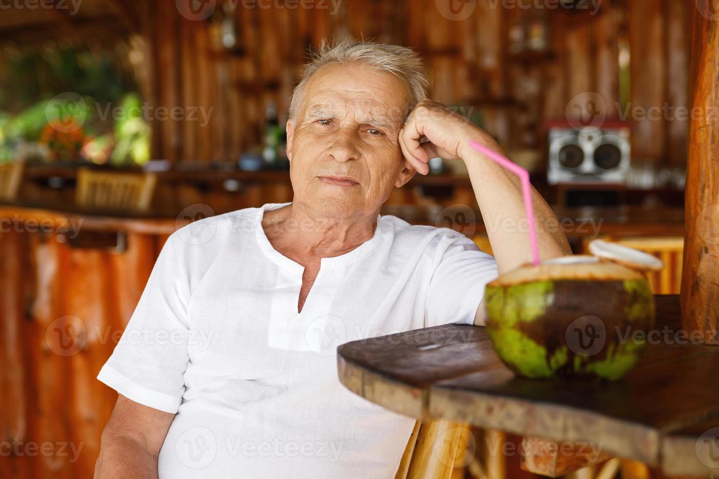 Happy senior man is drinking a coconut water in the beach bar photo