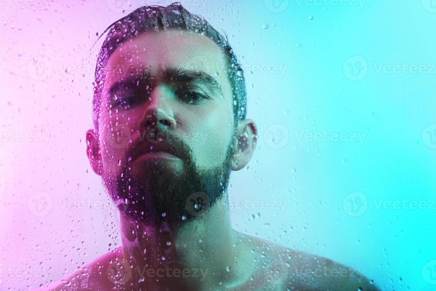 retrato de hombre guapo a través de vidrio mojado en luz de neón foto