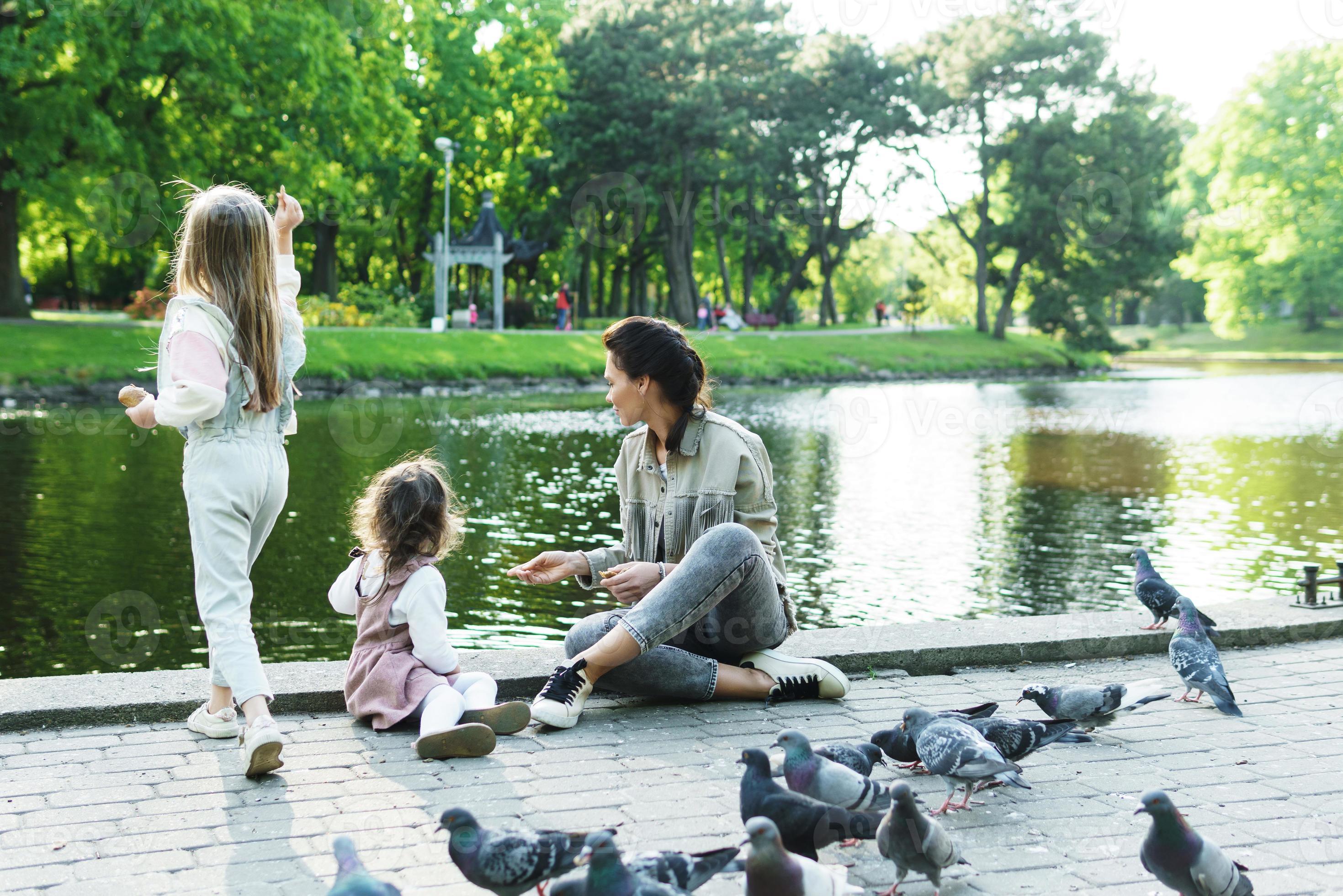 Mother and her little daughters feeding birds in city park 16248359