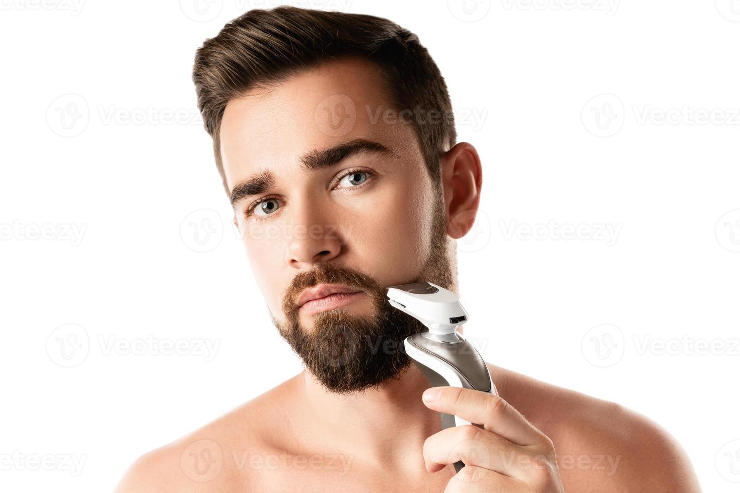 Handsome bearded man is using electric trimmer photo