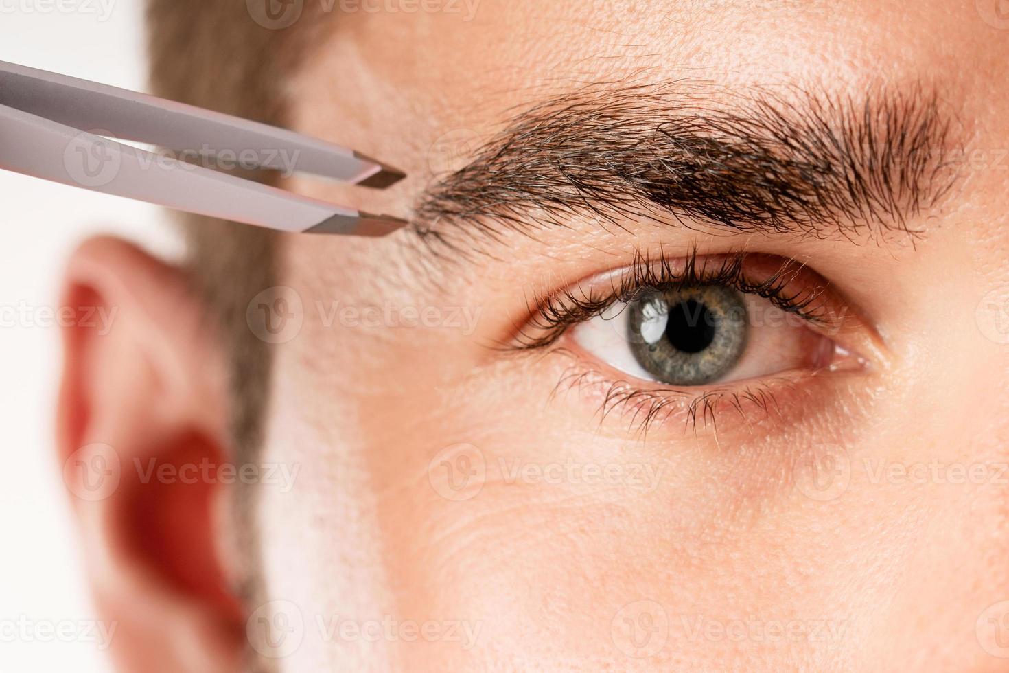 Male eye and tweezers for eyebrow grooming and shape correction photo