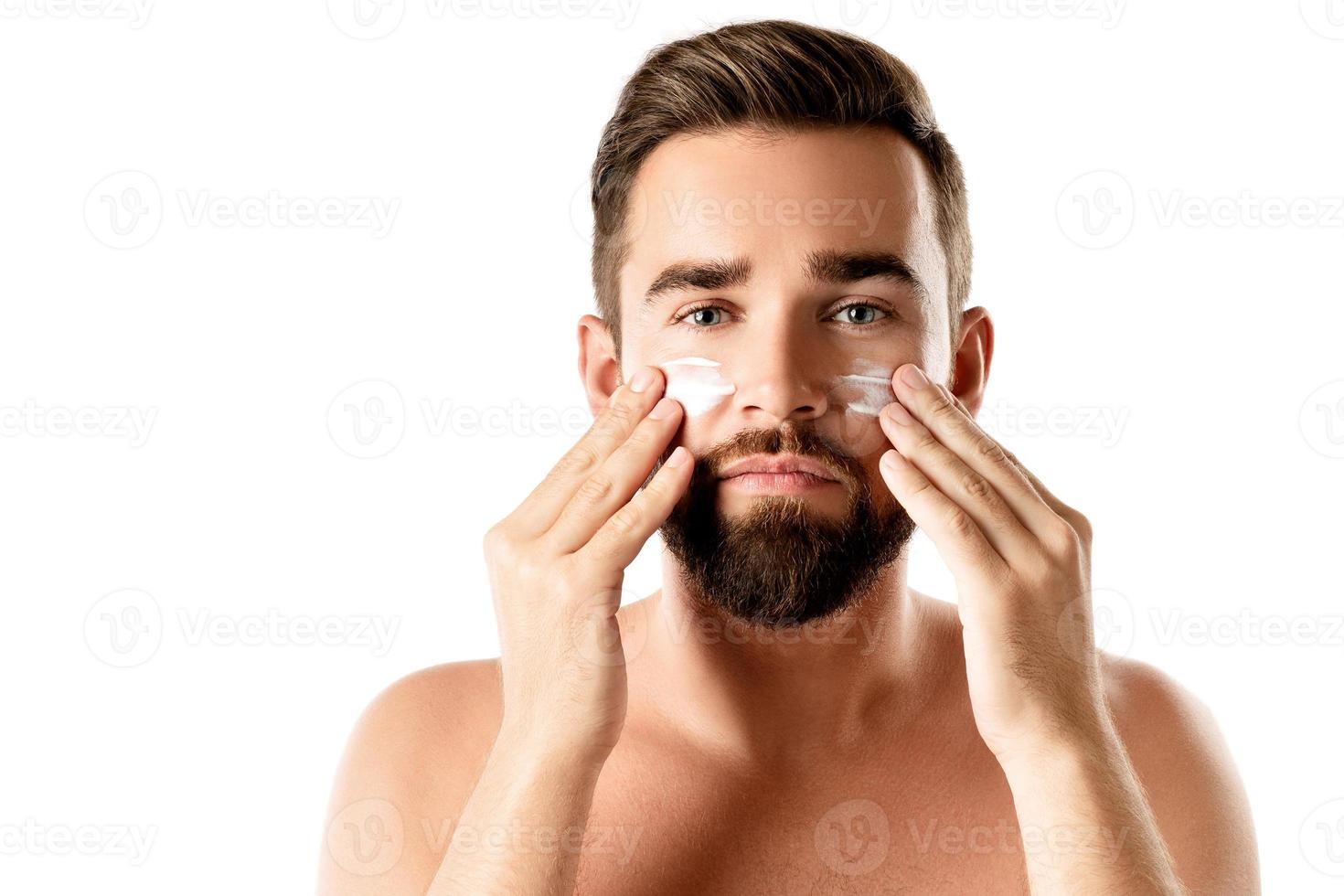 Young man is applying moisturizing and anti aging cream on his face photo