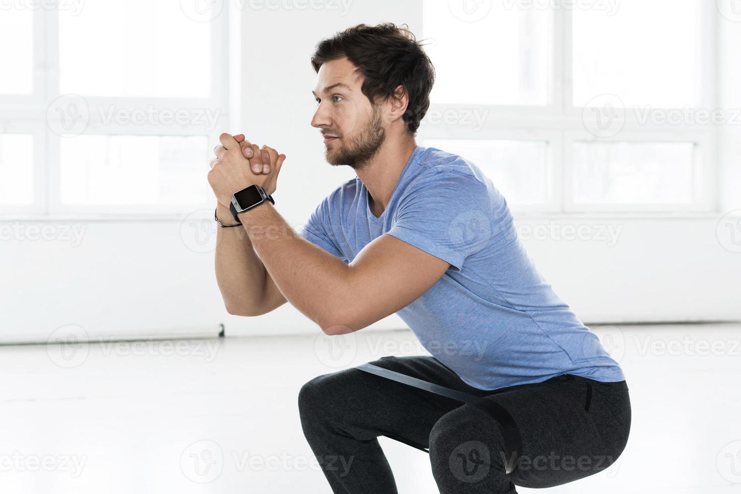 Man doing squats with a loop resistance band during workout in the gym photo