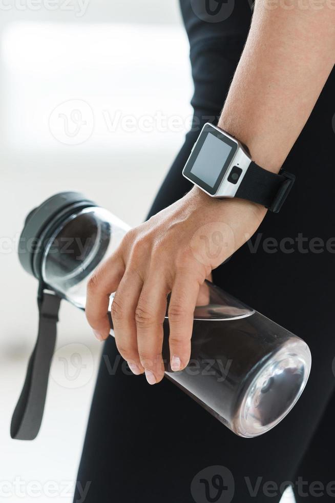 emale hand with smartwatch holding reusable bottle with water. photo