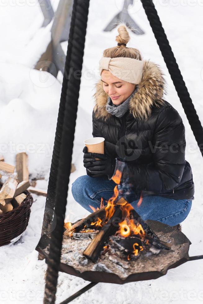 Beautiful woman warming up by the fire pit during cold winter day photo