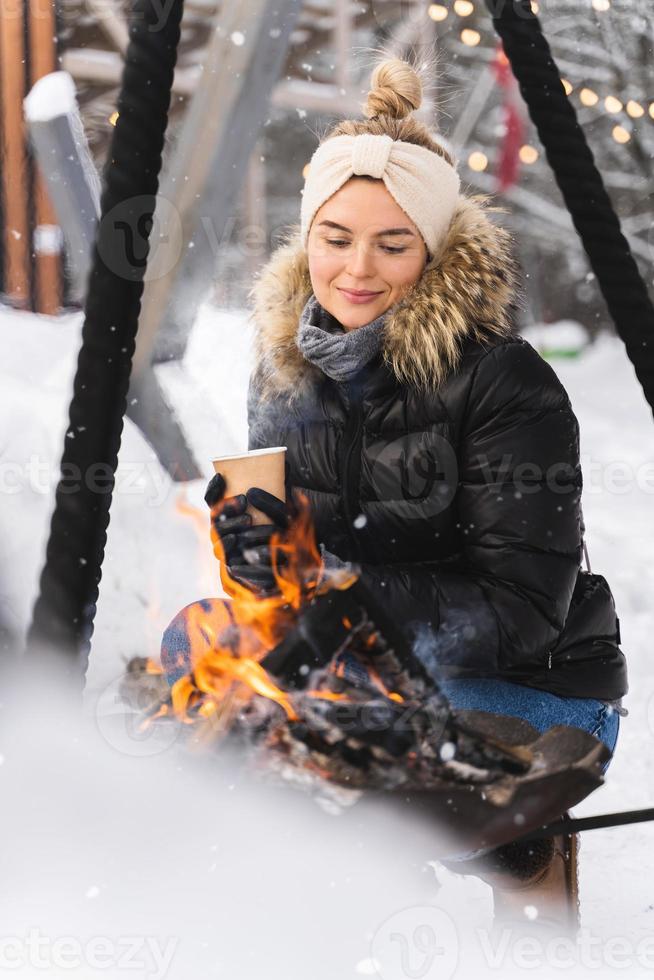 Beautiful woman warming up by the fire pit during cold winter day photo