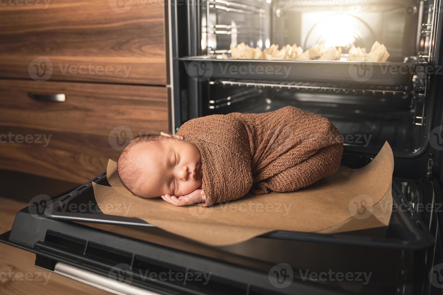 el bebé recién nacido está tirado en la bandeja del horno con muffins foto