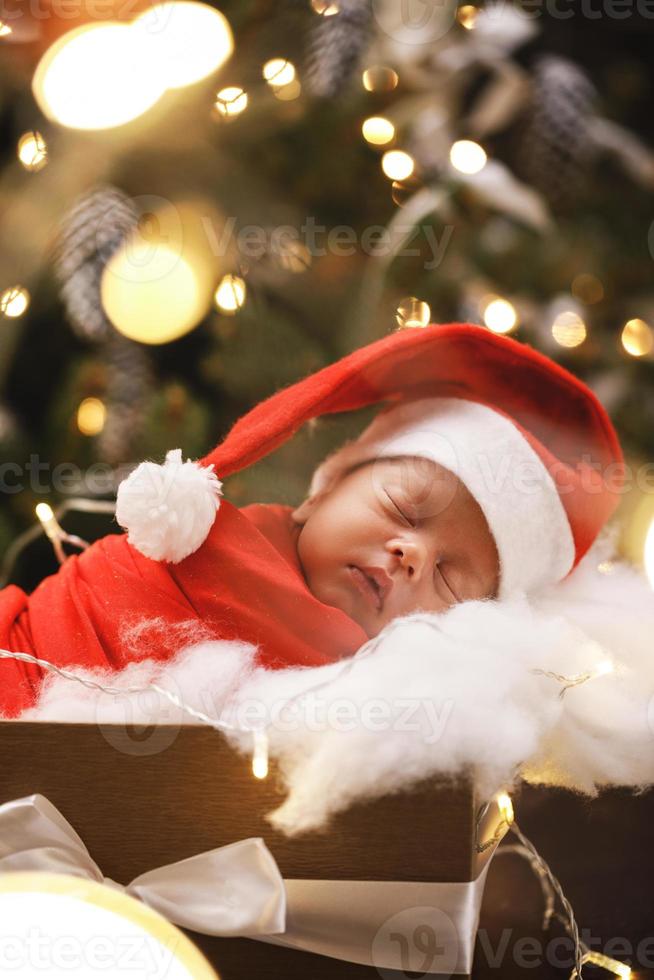 Cute newborn baby wearing Santa Claus hat is sleeping in the Christmas gift box photo