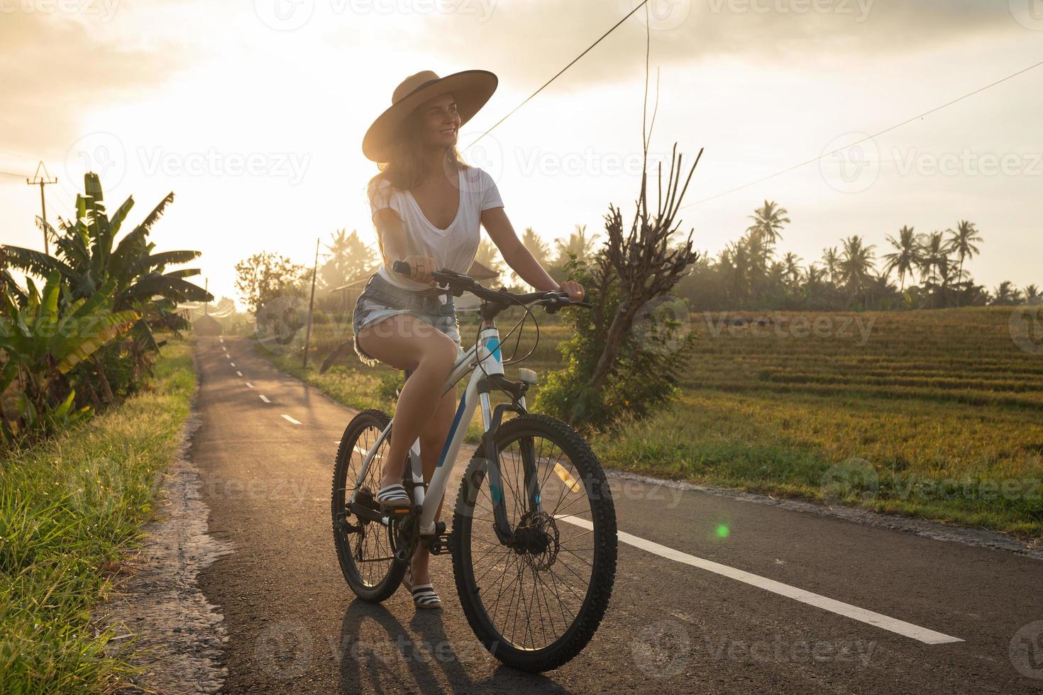 Woman is riding bicycle by narrow country road photo