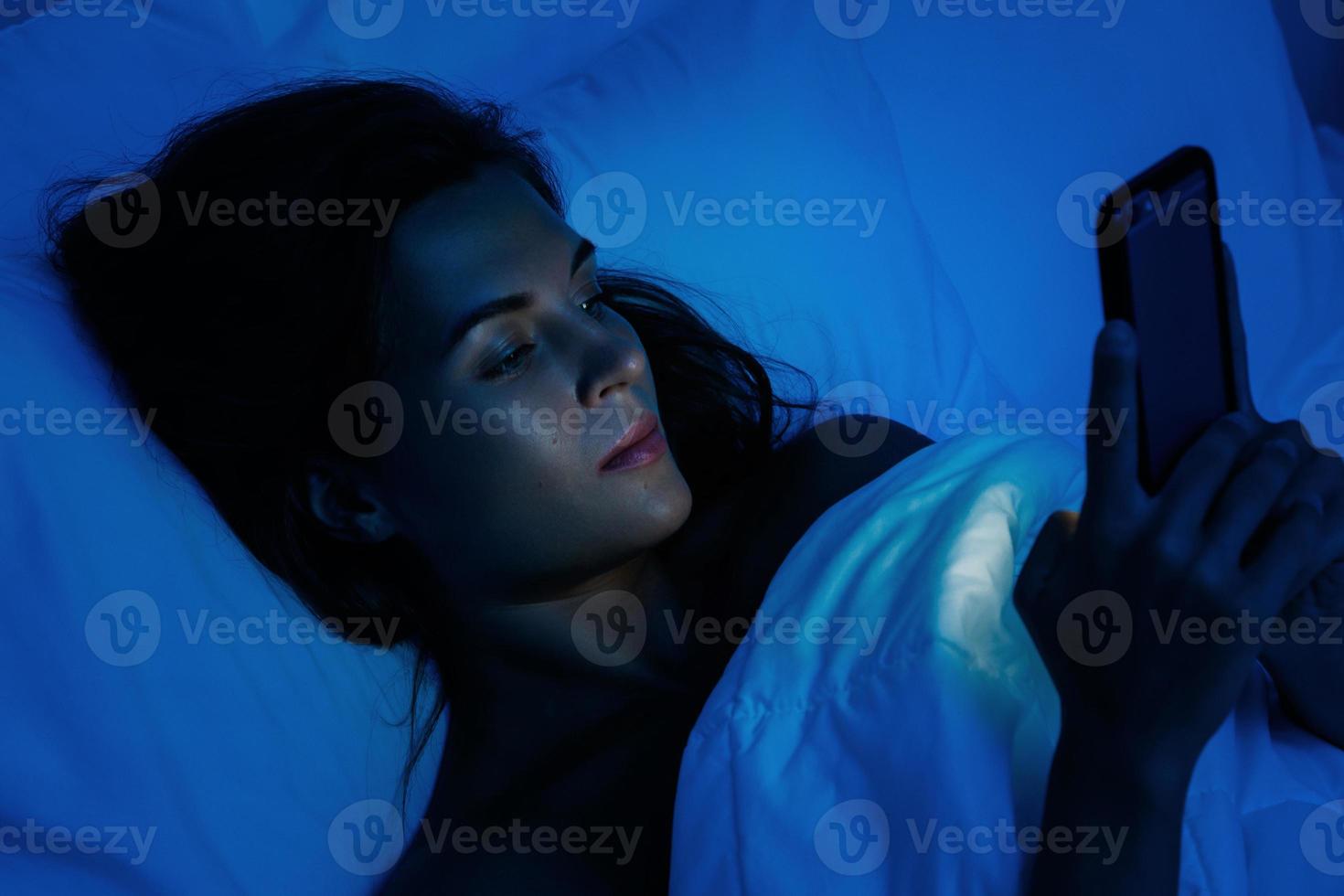 Young woman is using smartphone at night time in the bed photo