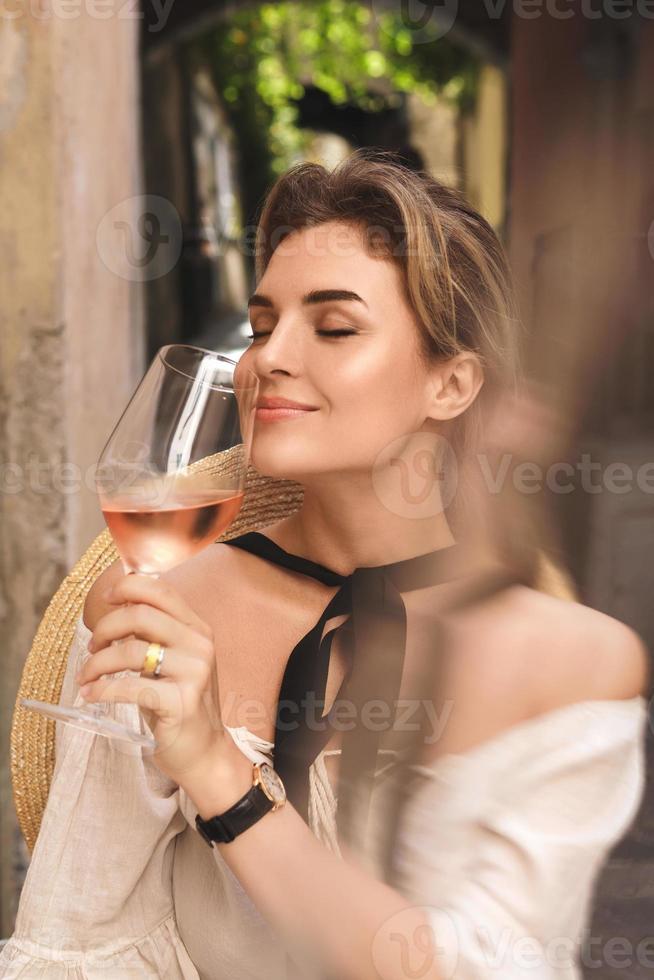 mujer joven está bebiendo vino rosado en el bar de la calle foto