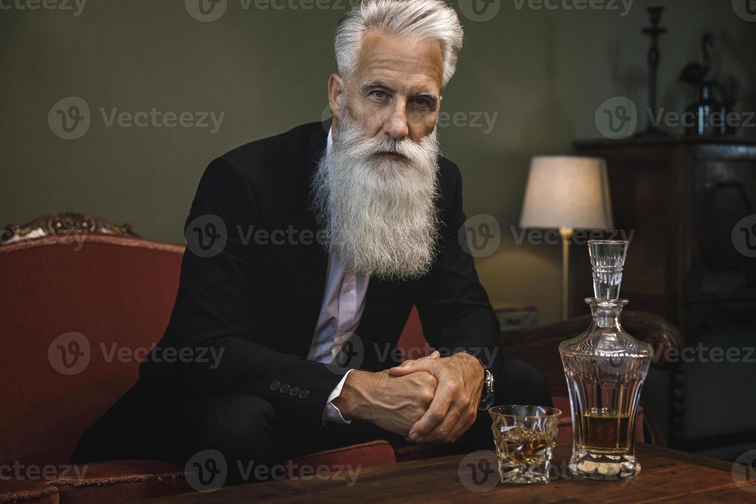 Handsome and bearded senior man drinking whiskey photo