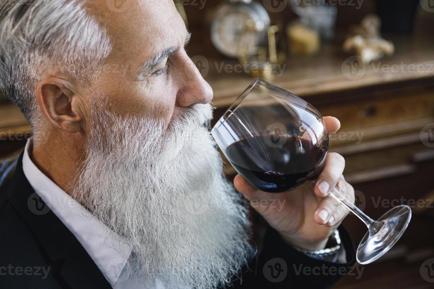 apuesto anciano barbudo bebiendo vino tinto foto