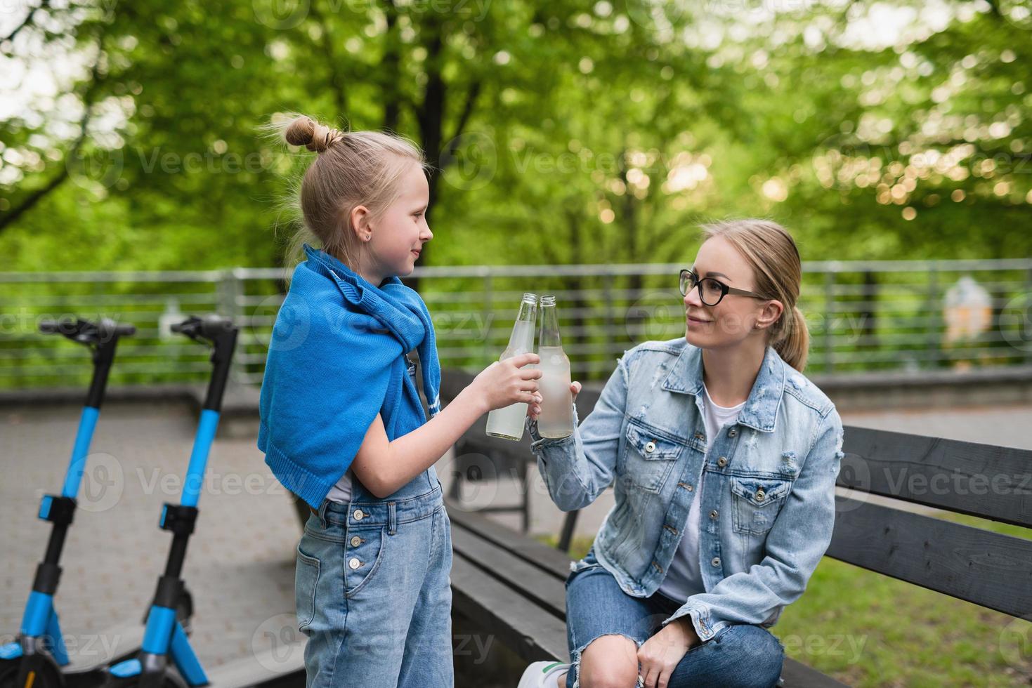Mother and daughter with electric scooters are drinking lemonade in city park photo