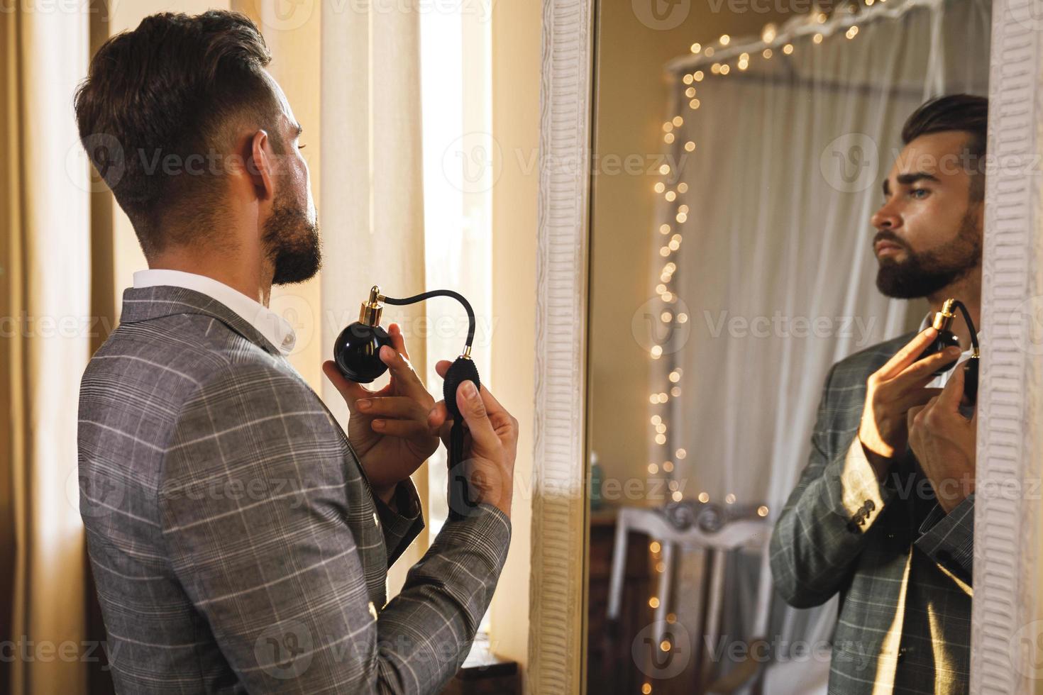 Handsome bearded man is using atomizer nozzle with perfume photo