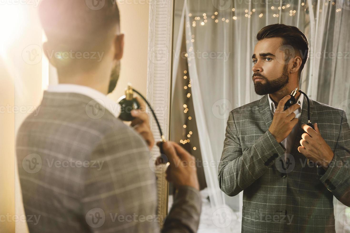 Handsome bearded man is using atomizer nozzle with perfume photo