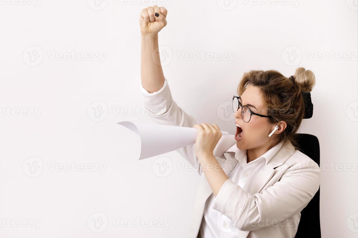 Motivated businesswoman shouting into the sheet of paper rolled like a loud speaker photo