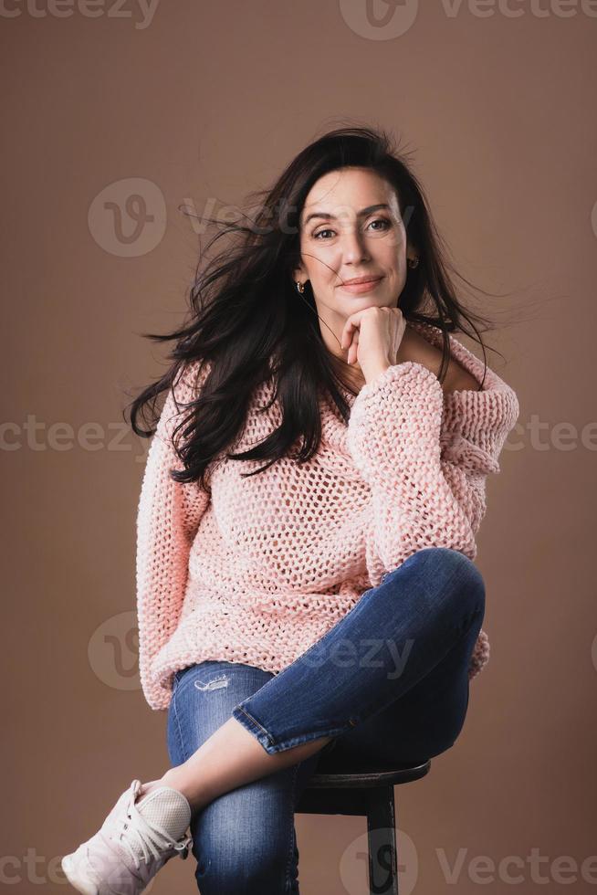 Beautiful middle aged woman wearing warm woolen sweater over brown background photo