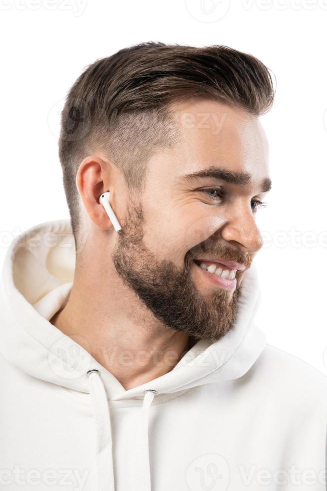 hombre guapo con barba vestido de blanco usando auriculares inalámbricos con fondo blanco foto