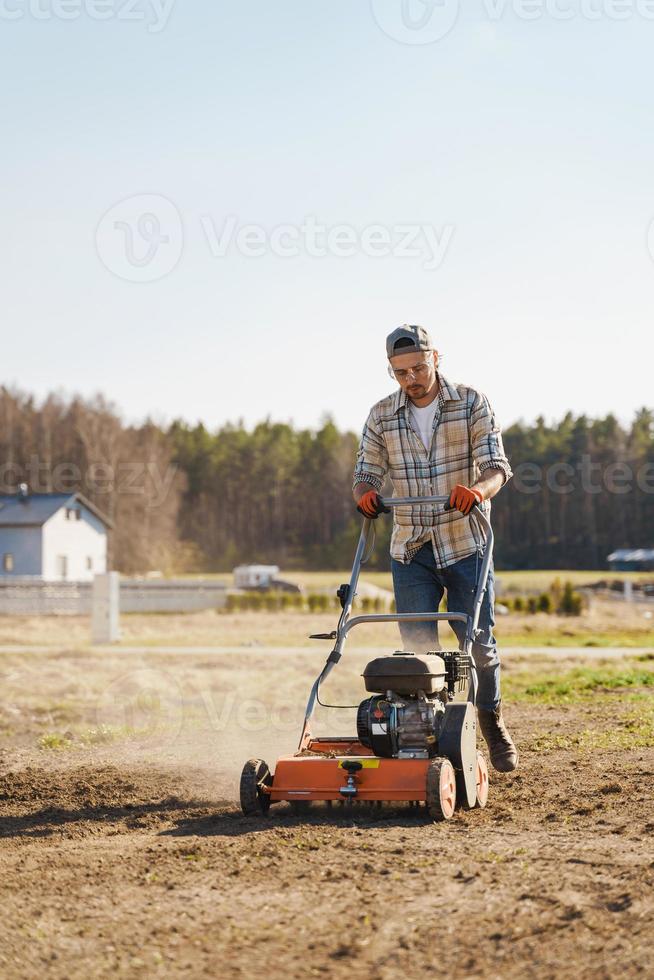 Man using aerator machine to scarification and aeration of lawn or meadow photo