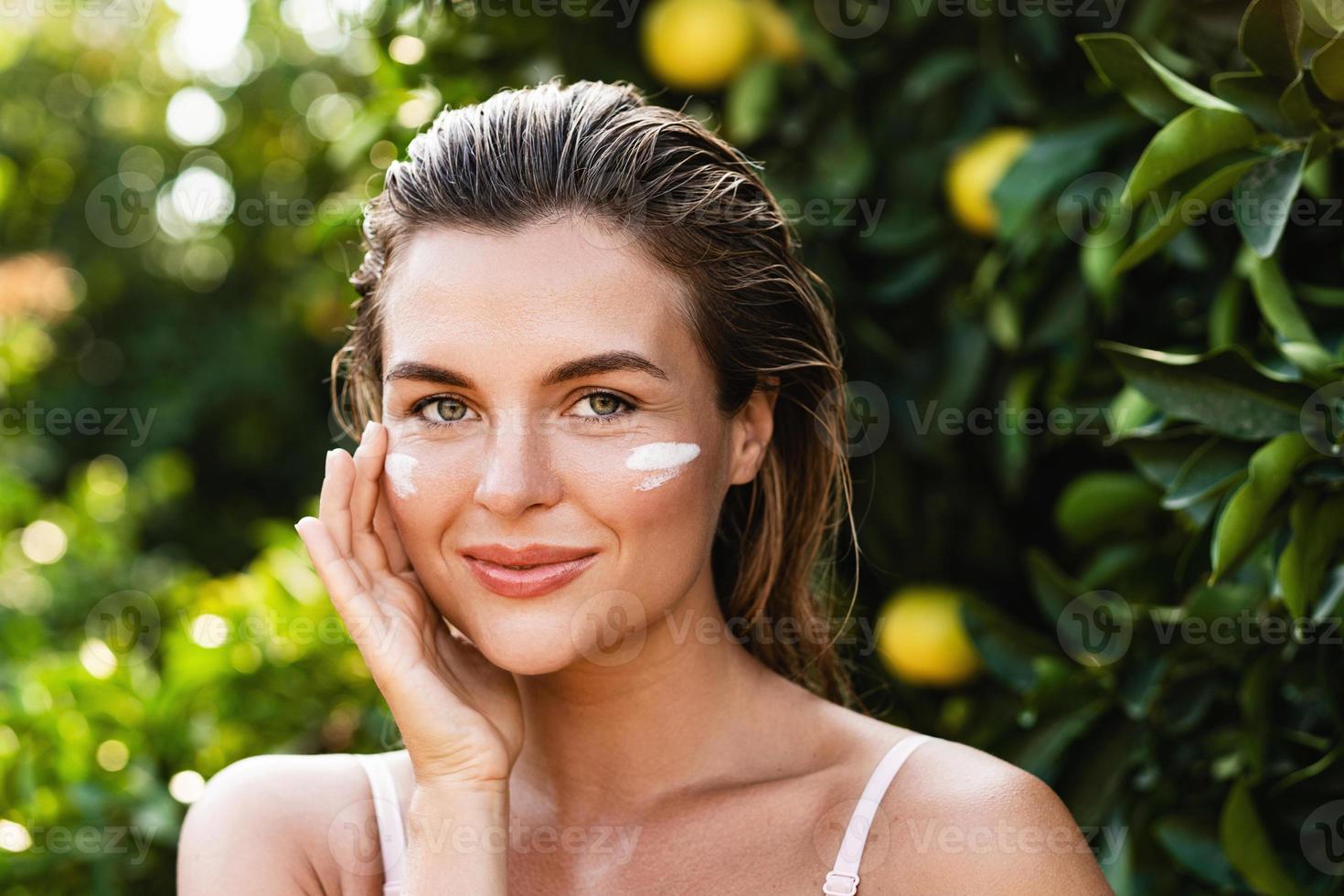 Beautiful woman with moisturizing cream under her eyes photo