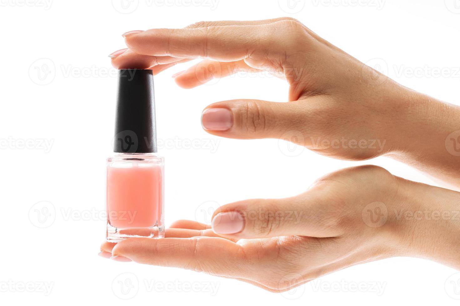 Female hands with beautiful french manicure holding bottle of pink nail polish against white background photo