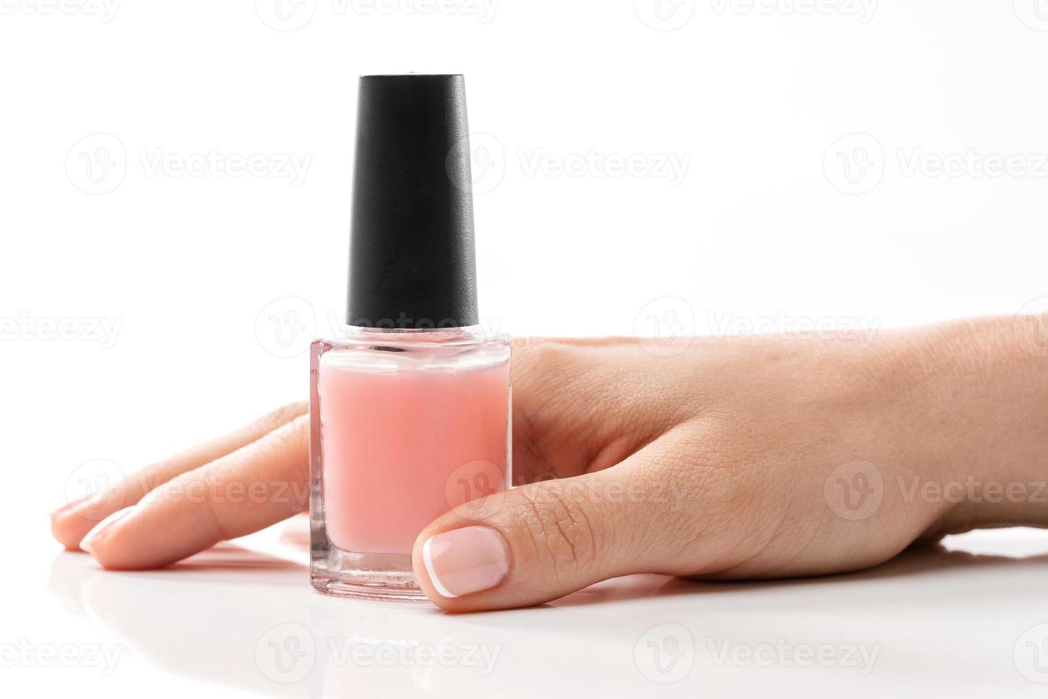 Female hand with beautiful french manicure holding bottle of pink nail polish against white background photo