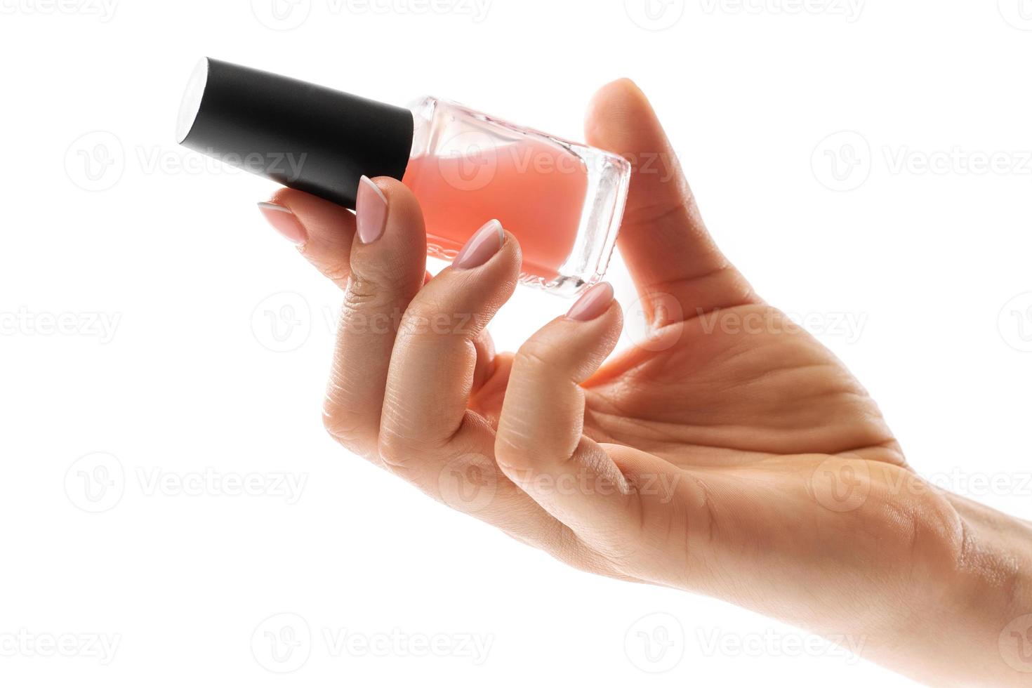 Female hand with beautiful french manicure holding bottle of pink nail polish against white background photo