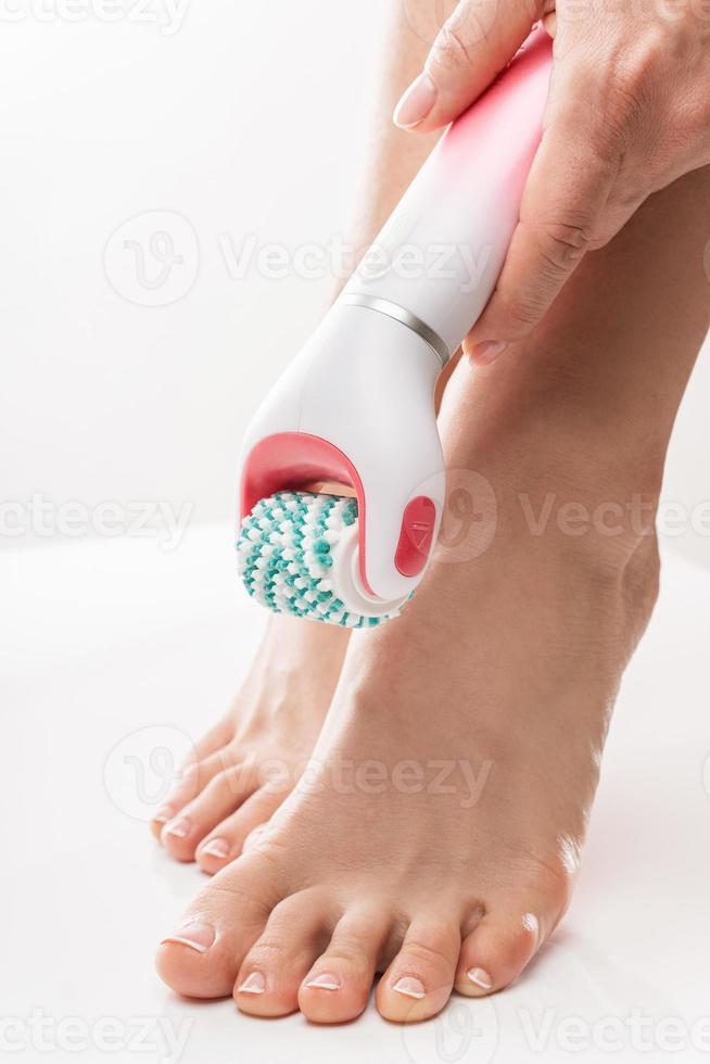 Female feet and electric foot scrubber or massage device on white