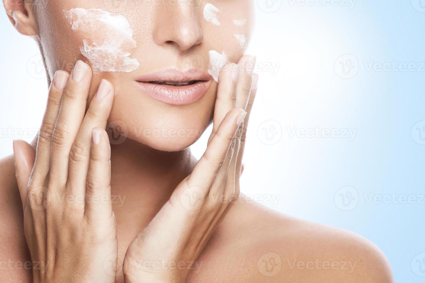 Beautiful woman applying moisturizing cream on her face photo