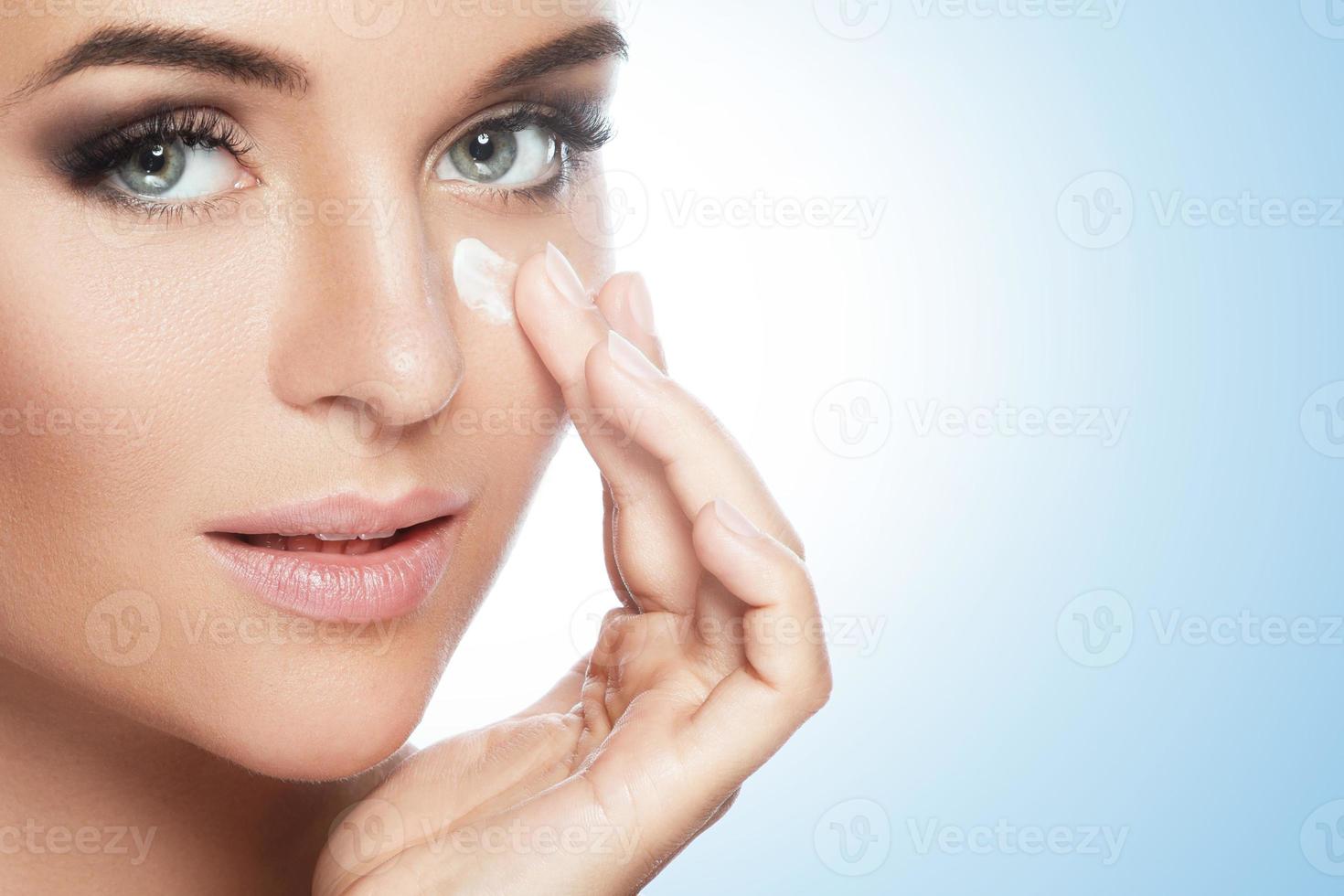 hermosa mujer aplicando crema hidratante debajo de su ojo foto