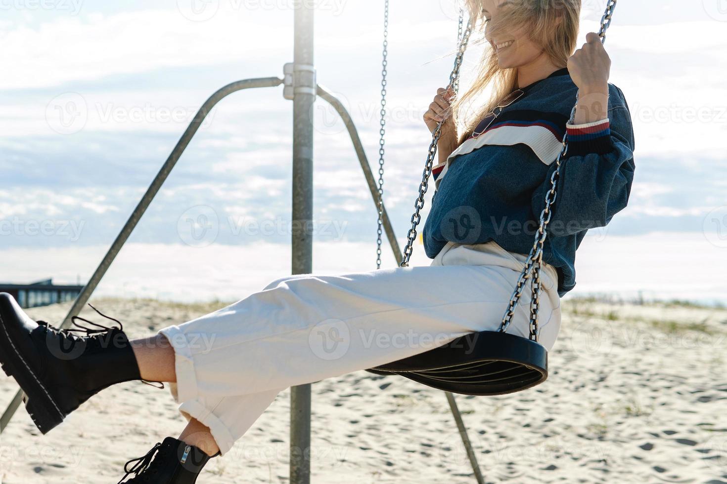 Young woman swinging on the swing and smiling at the sandy beach. photo