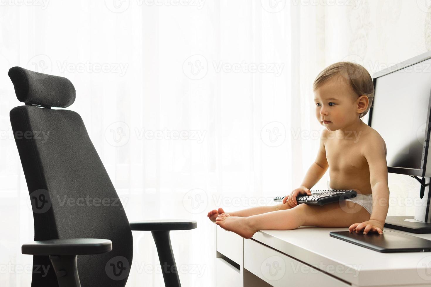 Little boy sitting on a desk and playing with a keyboard. photo