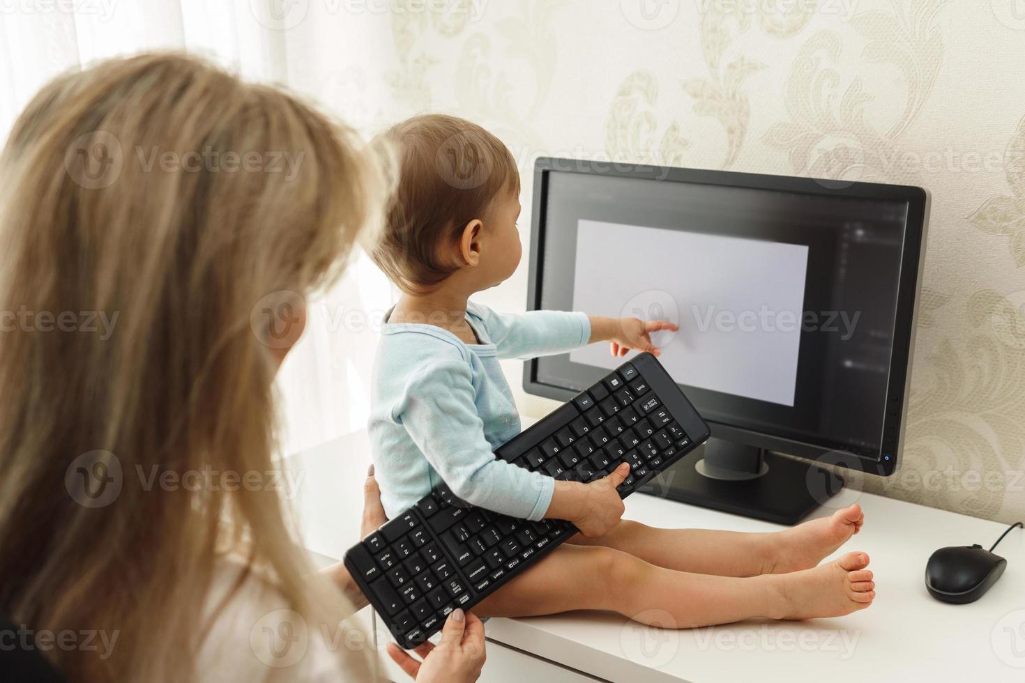 Little boy sitting on a desk and distracting mother from work on computer. photo