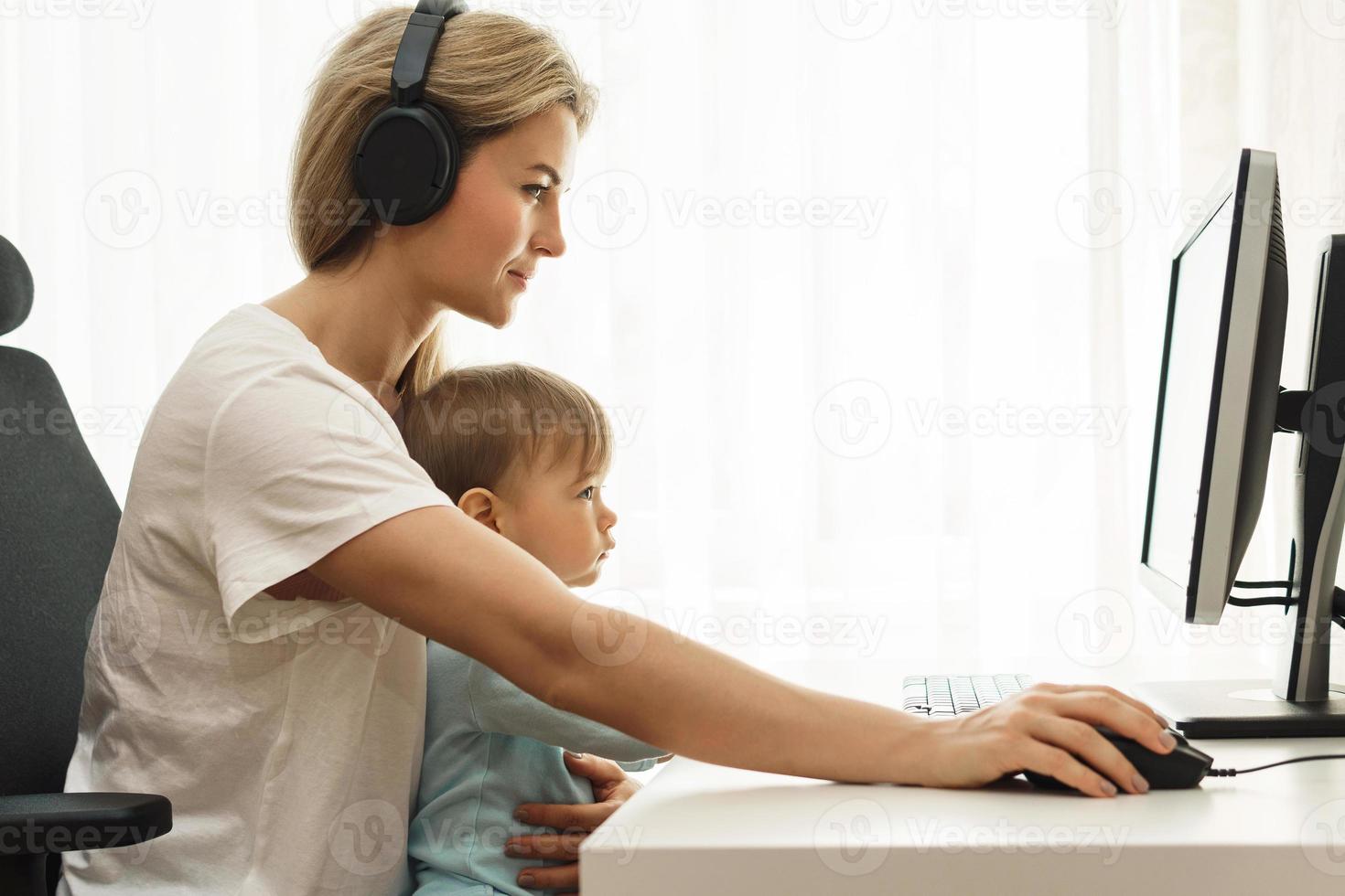 Young freelancer mother working on computer with son sitting on her lap. photo