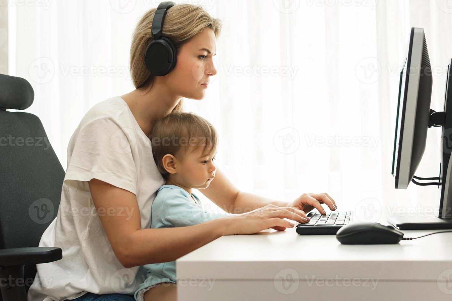 Young freelancer mother working on computer with son sitting on her lap. photo