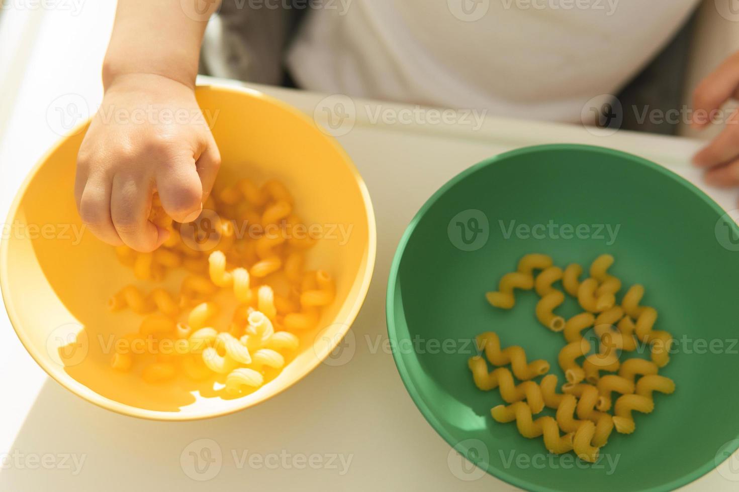 Closeup shot of little boy on high chair playing with uncooked pasta. photo